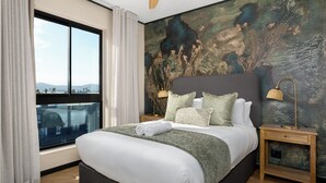 Ein Hotelzimmer mit einem großen Bett, einem Ausblick durch ein Fenster und einem Wandgemälde mit Struktur.