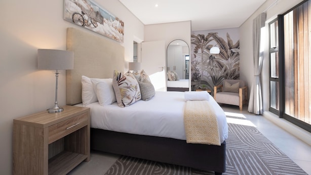 Ein modernes Schlafzimmer mit einem großen Bett, Nachttischen, einem Spiegel und Blick ins Freie.