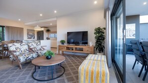 Ein modernes Wohnzimmer mit Fernseher, Sofa, Couchtisch und Essbereich.