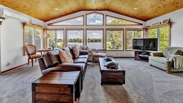 A spacious living room with a high ceiling, large windows, and a television. - Flip Flop Hideaway- Sandy beach for kids huge yard for dogs and fire pit for smores! (Huddleston)