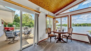 A spacious room with a large window overlooking a lake, a wooden ceiling, and a dining area with chairs and a table. - Flip Flop Hideaway- Sandy beach for kids huge yard for dogs and fire pit for smores! (Huddleston)