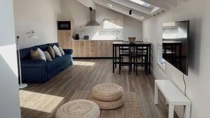 Ein modernes Wohnzimmer mit einem blauen Sofa, einem Esstisch mit Stühlen und einem an der Wand befestigten Fernseher.