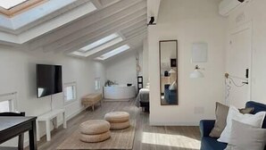 Ein geräumiges Loft mit hohen Decken, Dachfenstern, einem großen Spiegel, einem blauen Sofa und einer hölzernen Bank.