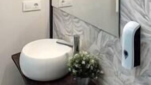 Ein Badezimmer mit einem runden, weißen Waschbecken, einem Spiegel mit Beleuchtung und einer Seifenspender.