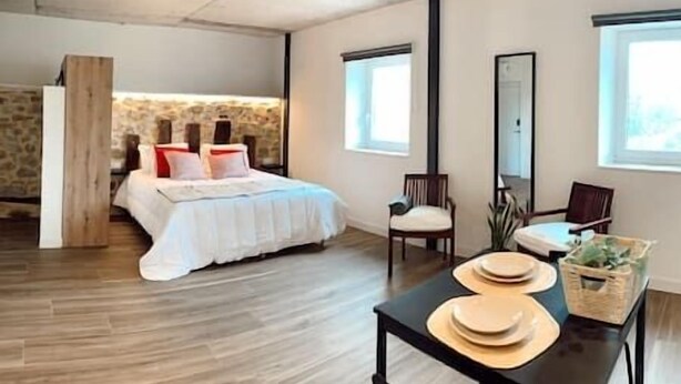 Ein Schlafzimmer mit Steinwand, einem Bett mit weißer Bettwäsche, Holzboden, einem Sessel, einem Tisch mit Tellern und einem Spiegel.