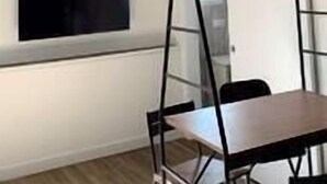 Ett rum med ett vitt tak, en tv som är monterad på väggen, ett bord med stolar och ett fönster.