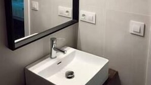 Une salle de bain avec un lavabo blanc, un miroir avec éclairage intégré et un interrupteur fixé au mur.