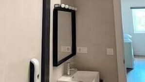 Une salle de bain avec un lavabo blanc, un miroir et une porte donnant sur une autre pièce.