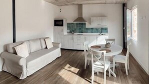 Una sala de estar moderna con un sofá y una mesa de comedor con sillas. Hay una zona de cocina con armarios y una estufa.
