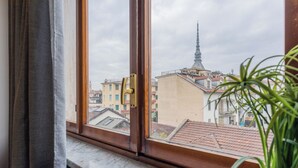 A window with a view of a building with a spire, a balcony, and a potted plant on the windowsill. - Casa Antonelli by Wonderful Italy (Turin)