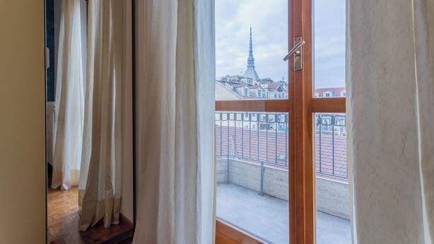 A room with a large window overlooking a cityscape, featuring a prominent tower and a bridge. - Casa Antonelli by Wonderful Italy (Turin)