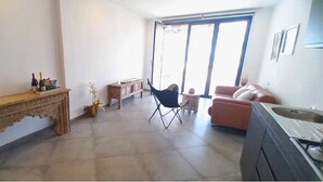 Un salón amplio con una consola de madera, un sofá, una silla plegable y un ventanal que proporciona luz natural.