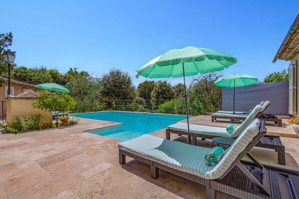 Una piscina con sillas de descanso y sombrillas verdes.