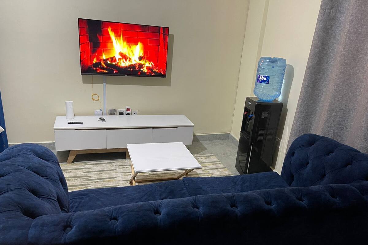 A living room with a TV displaying a fireplace, a water dispenser, and a sofa.