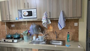 Una cocina con gabinetes de madera, microondas, estufa, fregadero y diversos utensilios y electrodomésticos.