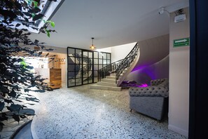 Un intérieur moderne avec un sol en terrazzo, un escalier doté d’une rampe en verre et un coin salon agrémenté d’un canapé capitonné.