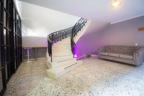 Eine Treppe mit schwarzer Geländer führt zu einer Zwischenebene, wo ein gestepptes Sofa und ein Barhocker in einem Raum mit punktierten Boden stehen.