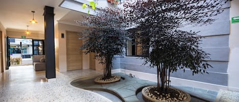 A spacious indoor area with a terrazzo floor, two potted trees, and a view of the outside through a glass wall.