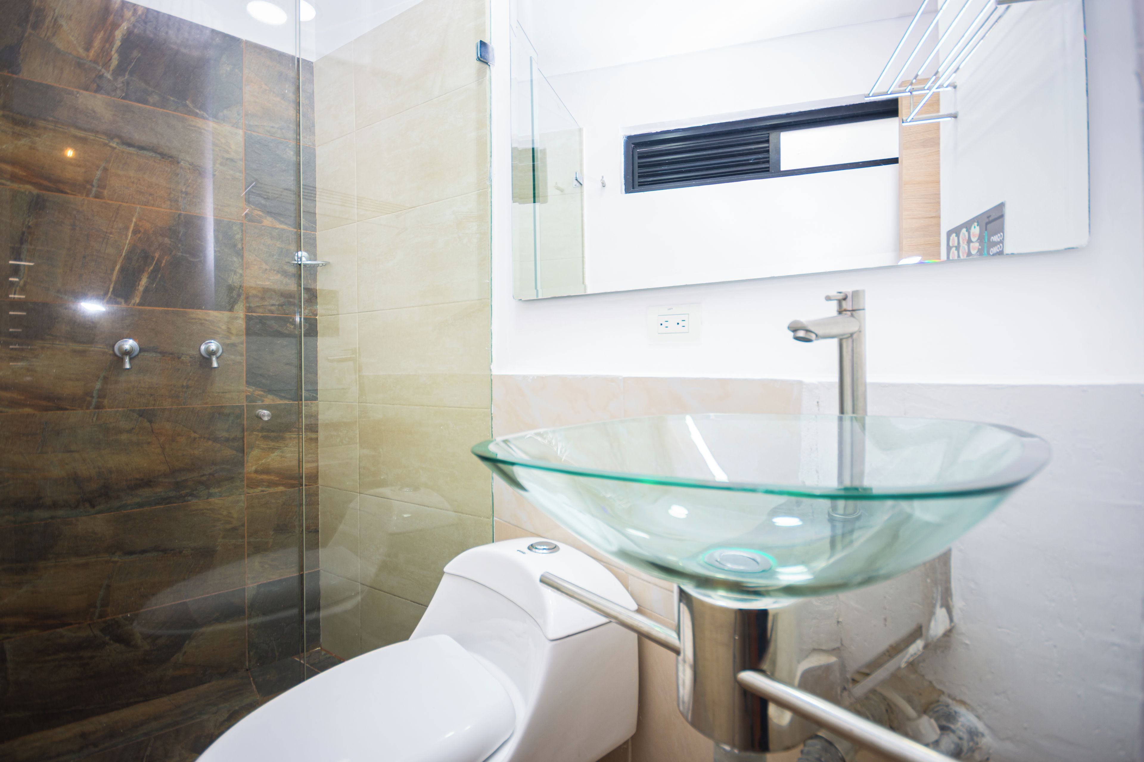 A modern bathroom with a glass sink, a shower enclosure, and a toilet.