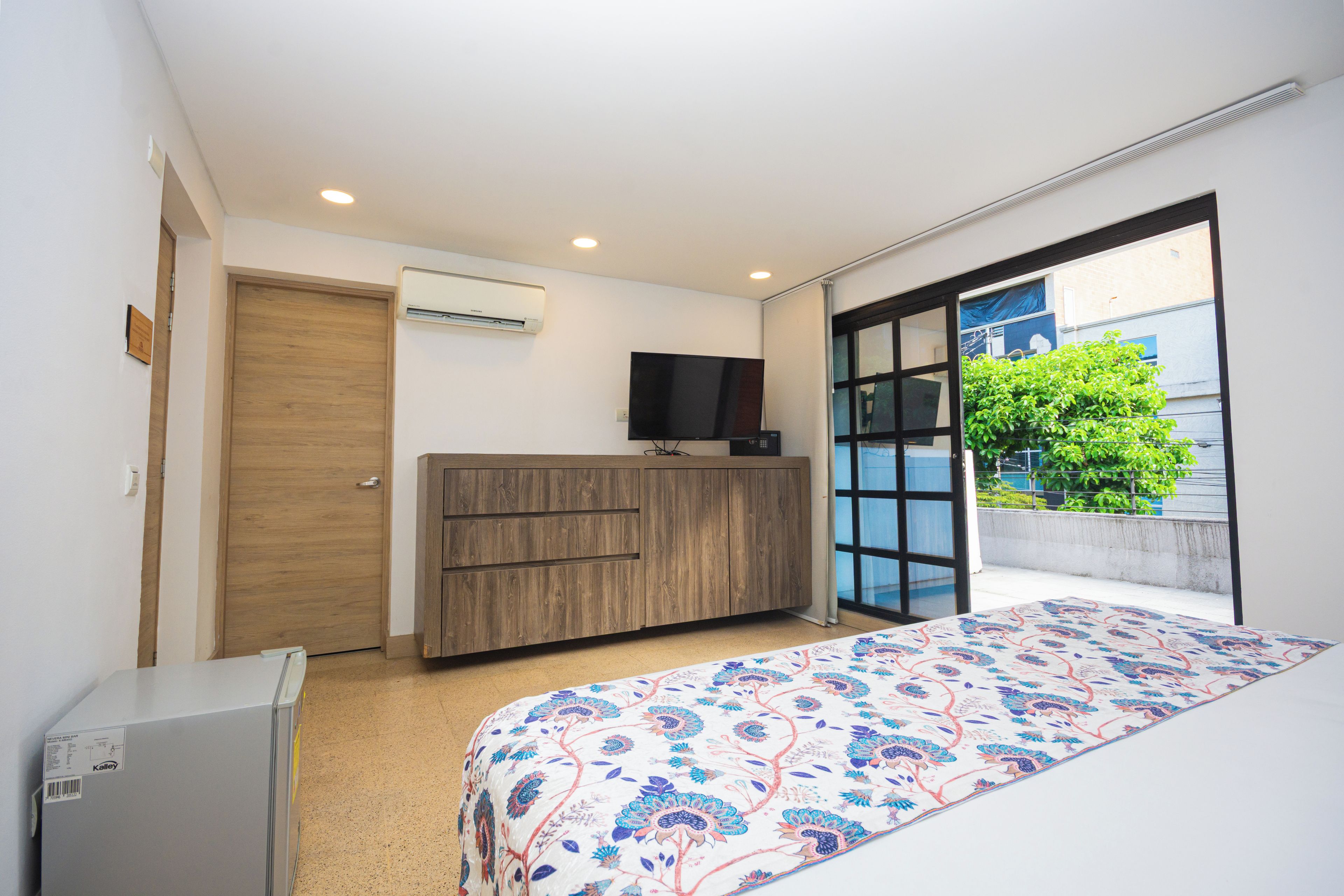 Een slaapkamer met een bed, een houten dressoir, een televisie en een airconditioner.