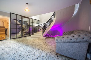 A modern interior with a terrazzo floor, a staircase with a glass railing, and a tufted sofa. - POMAROSA (Medellín)
