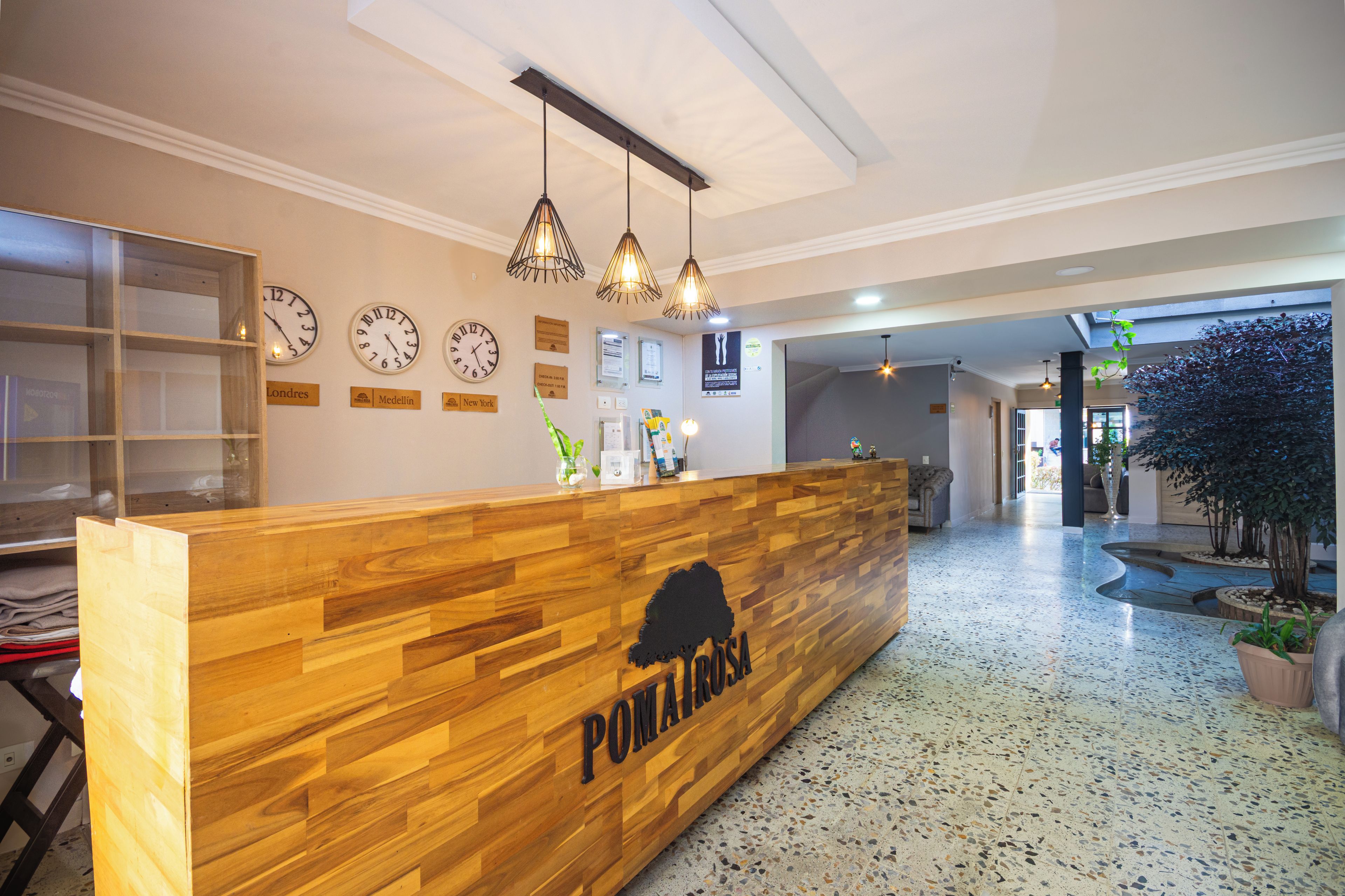 Un mostrador de recepción con detalles de madera y un logotipo en silueta negra. Hay relojes de pared y una vitrina de vidrio con objetos.