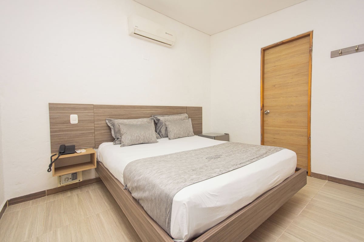 A neatly arranged bedroom with a wooden headboard, a bed with a grey blanket, a bedside table with a phone, and a wooden door.