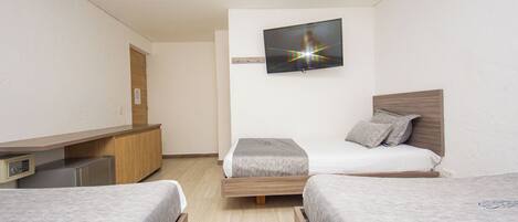 Een hotelkamer met twee enkele bedden, een aan de muur bevestigde televisie, een houten bureau en een kleine koelkast.
