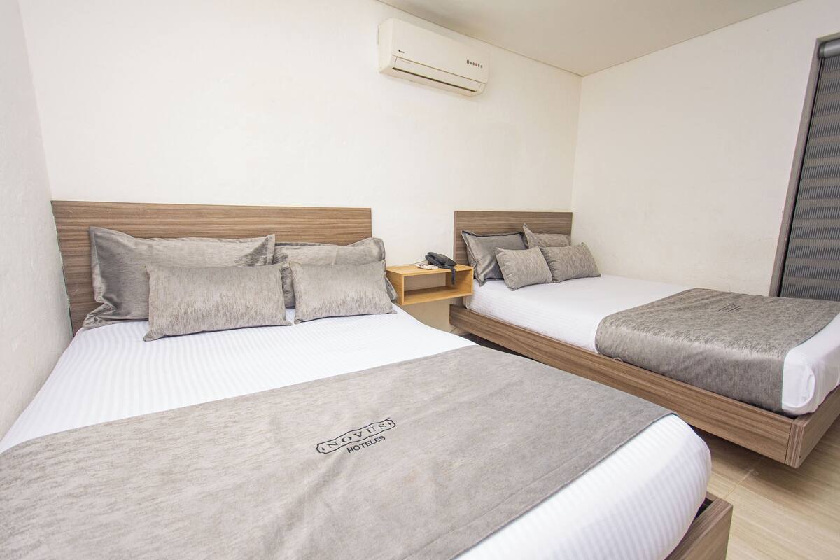 A hotel room with two single beds, each with a wooden headboard, a bedside table, and a grey blanket.