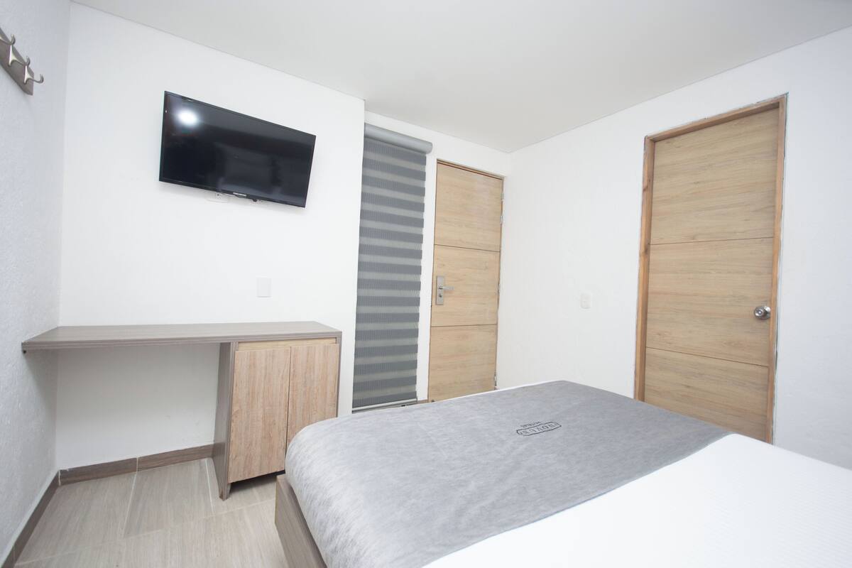 A bedroom with a bed, a desk, a TV, and two doors.