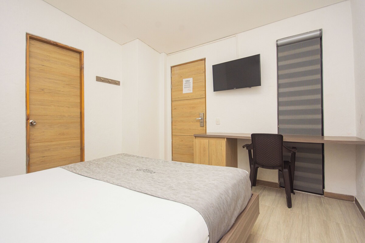 A bedroom with a bed, a desk, a chair, a TV, and a radiator.