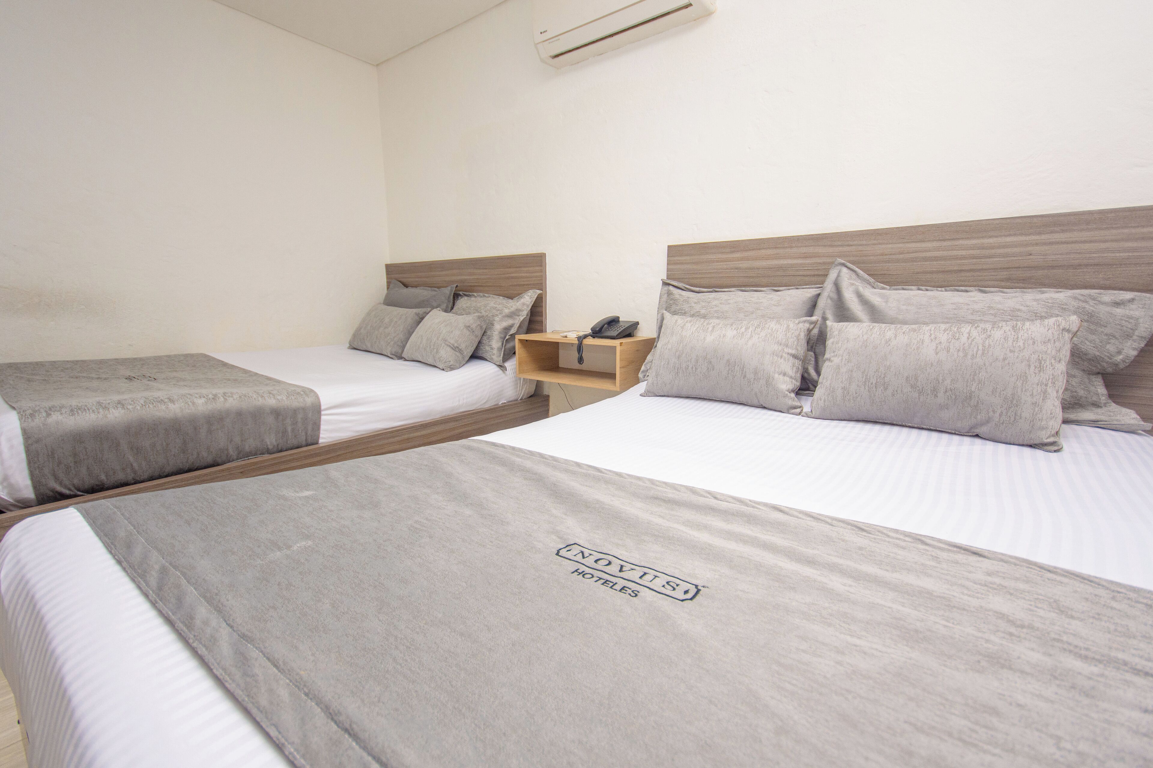 A hotel room with two beds, each with a grey bedspread and matching pillows. There is a wooden nightstand with a phone between the beds.