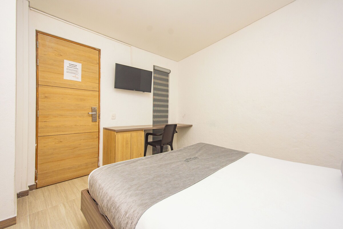 A bedroom with a bed, a desk, a chair, and a TV on the wall.