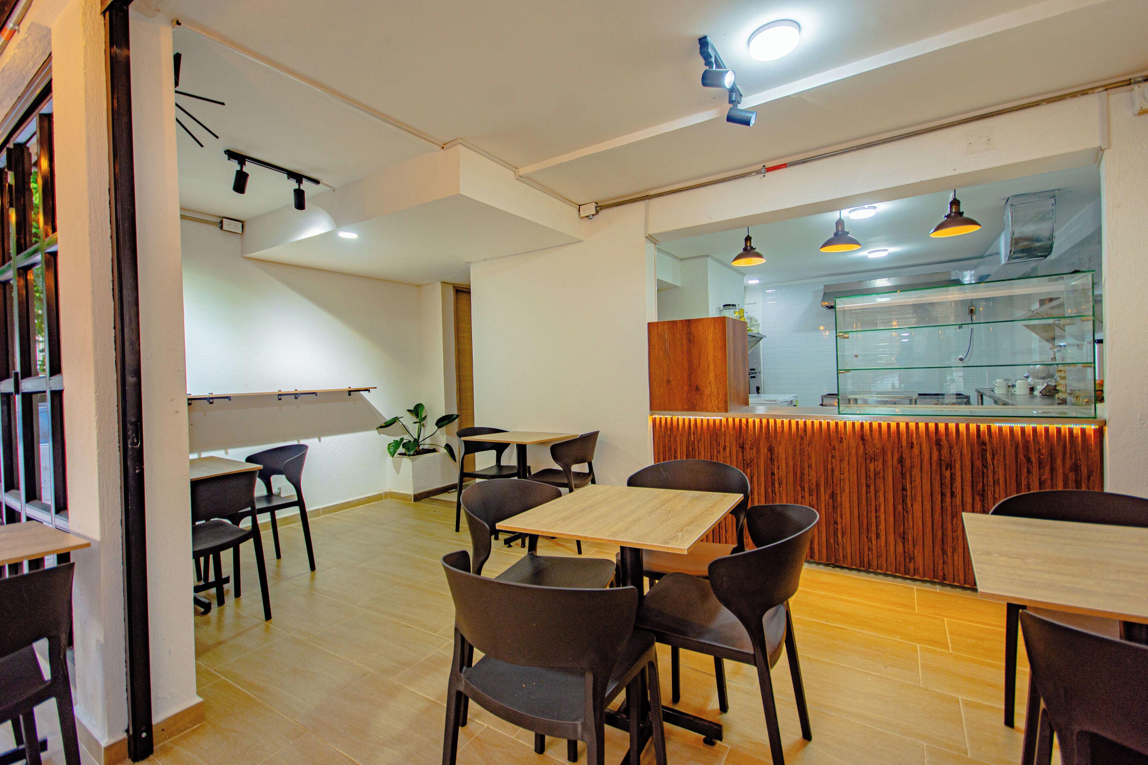 A restaurant interior with wooden tables and chairs, a kitchen area with glass display cases, and pendant lighting.