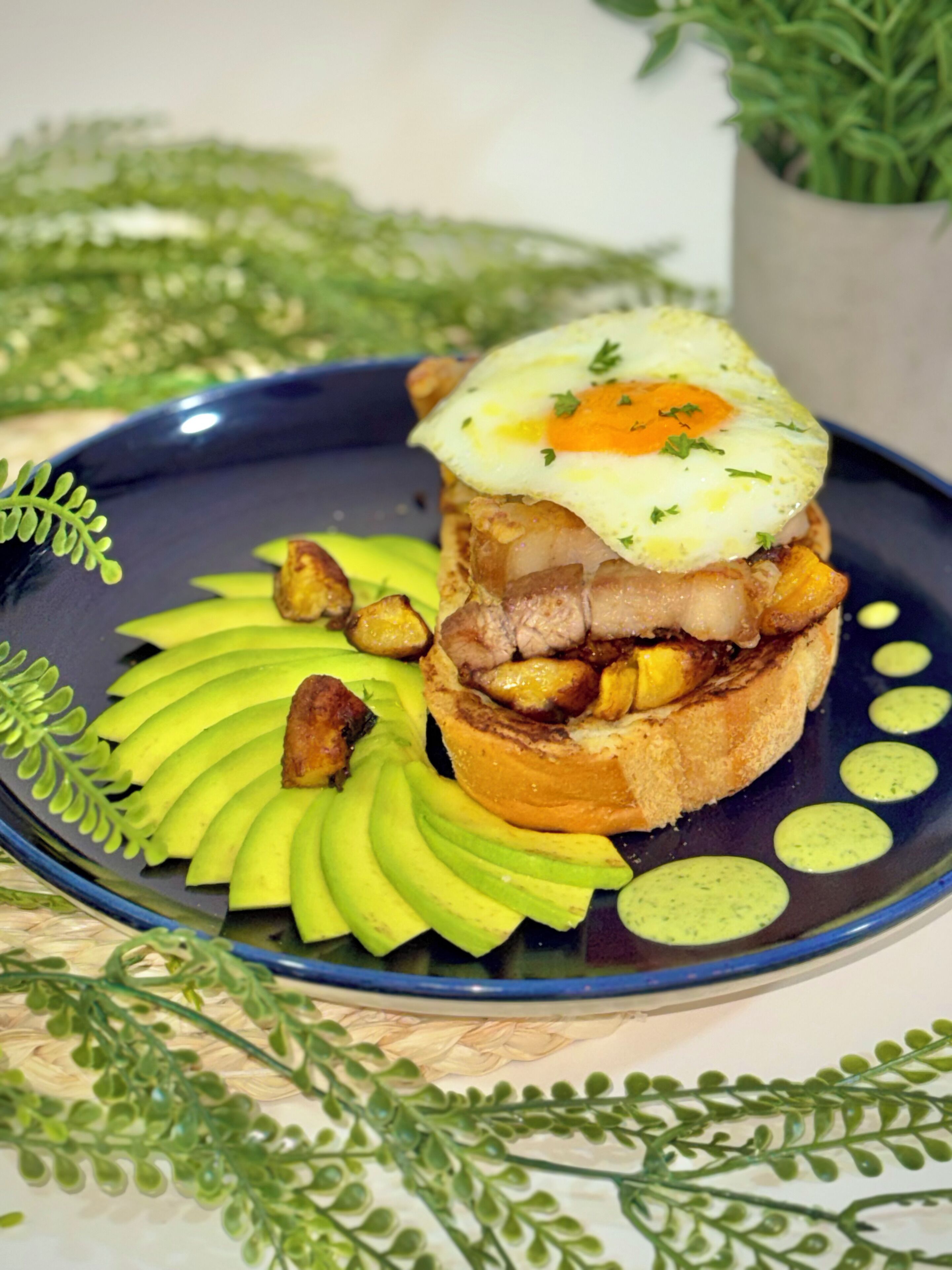 Een bord met een sandwich, plakjes avocado en een gebakken ei op een blauw bord.