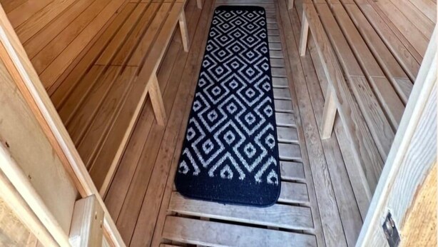 Eine Sauna mit Holzwänden und -bänken, einer gemusterten Matte und einem kleinen Fenster.