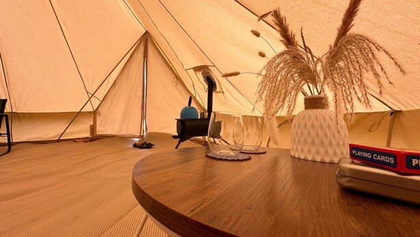 A tent interior with a round wooden table, a portable stove, and a glass of water.