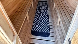A sauna with wooden walls and benches, a patterned mat, and a small window.