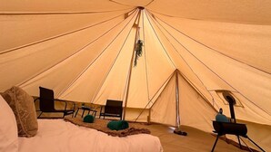 A tent with a bed, chairs, and a grill.