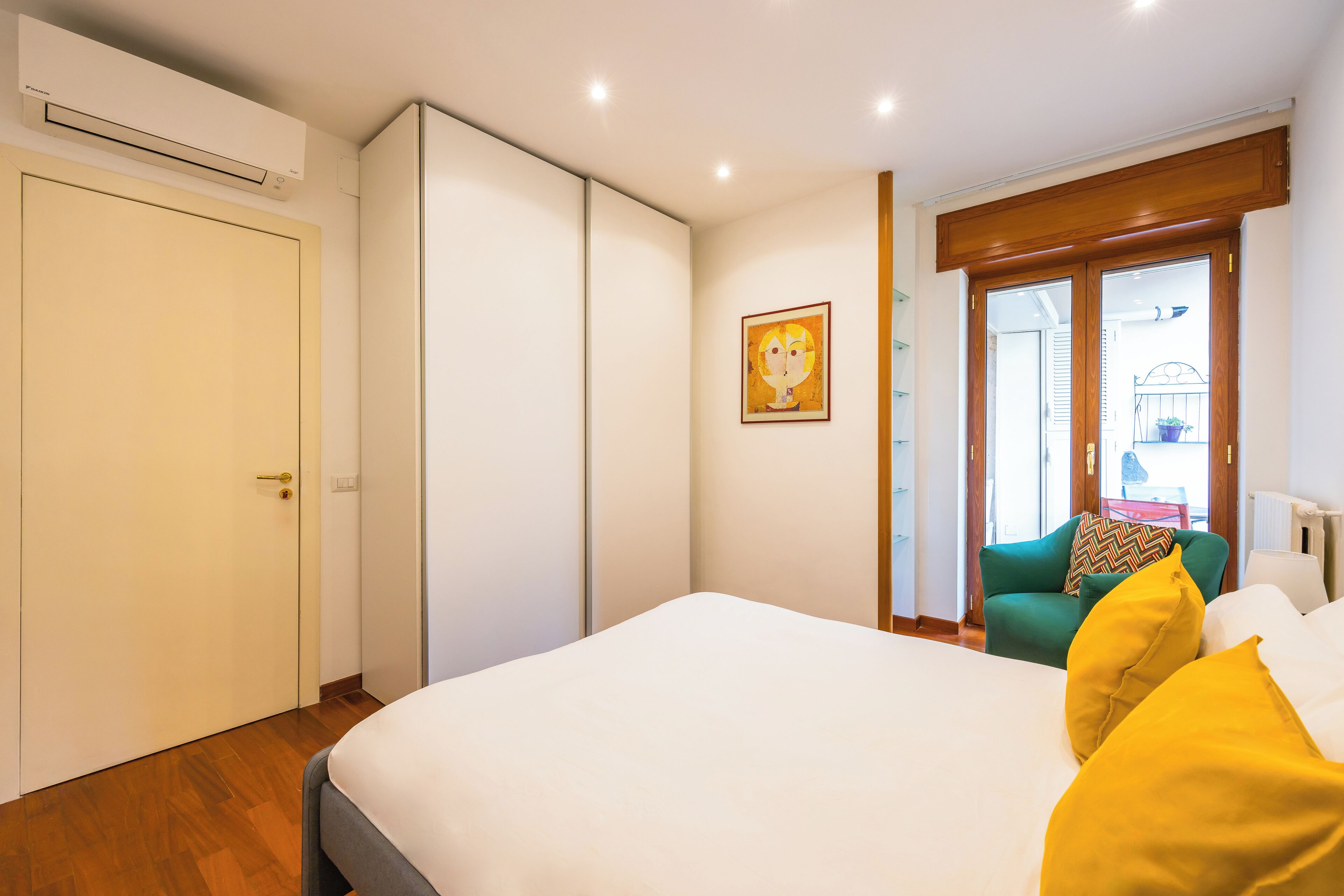 Een slaapkamer met een bed, een groene stoel, een raam en een deur.
