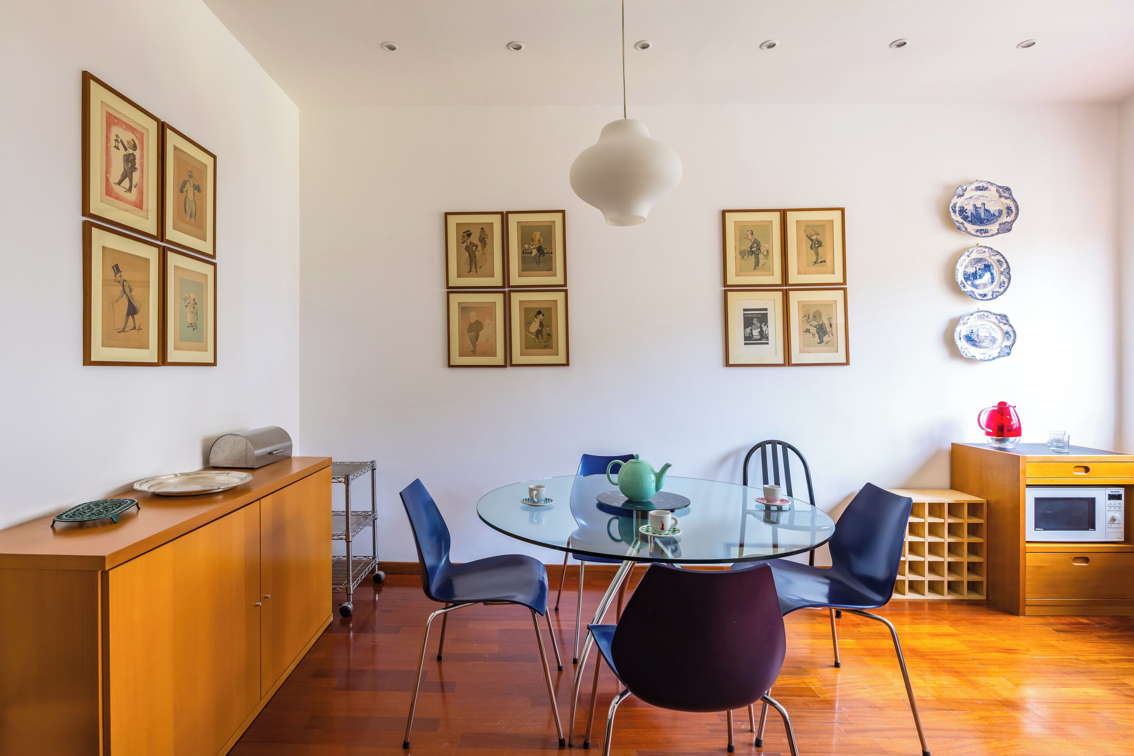 Un espace repas moderne avec une table en verre, quatre chaises, un meuble et des œuvres d’art accrochées au mur.