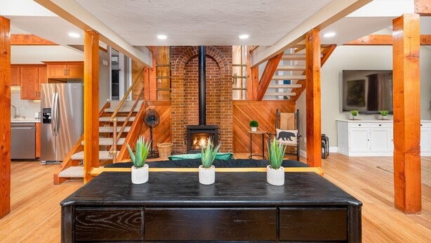 Ein geräumiger Wohnbereich mit Kamin, Holzbalken, einer Treppe und einer modernen Küche.