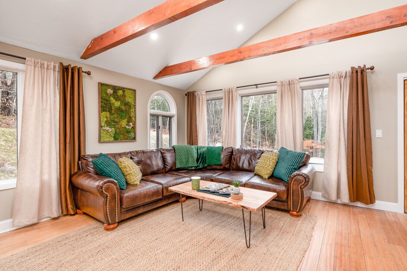 A living room with a brown leather sectional sofa, a wooden coffee table, and large windows with curtains.