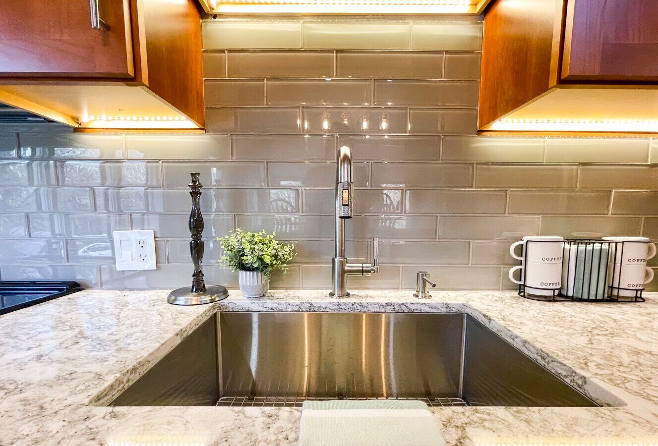 A kitchen with a stainless steel sink, a potted plant, and a coffee station.