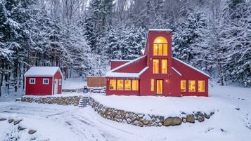 A red building with a stone wall and a smaller red structure nearby, surrounded by snow-covered trees.