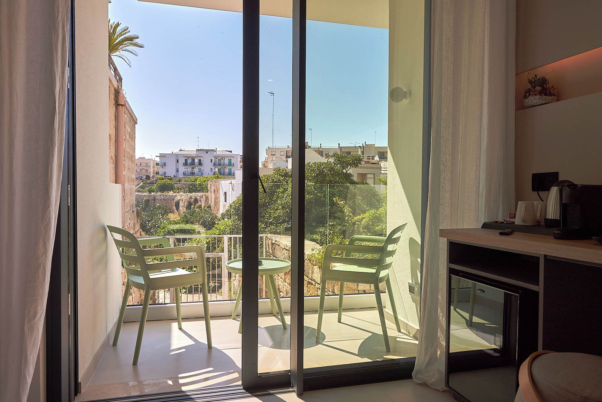 A balcony with two chairs and a table, overlooking a residential area with buildings and greenery.
