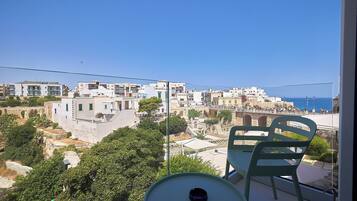 A balcony with a table and chairs overlooking a coastal town with white buildings and a clear blue sky.