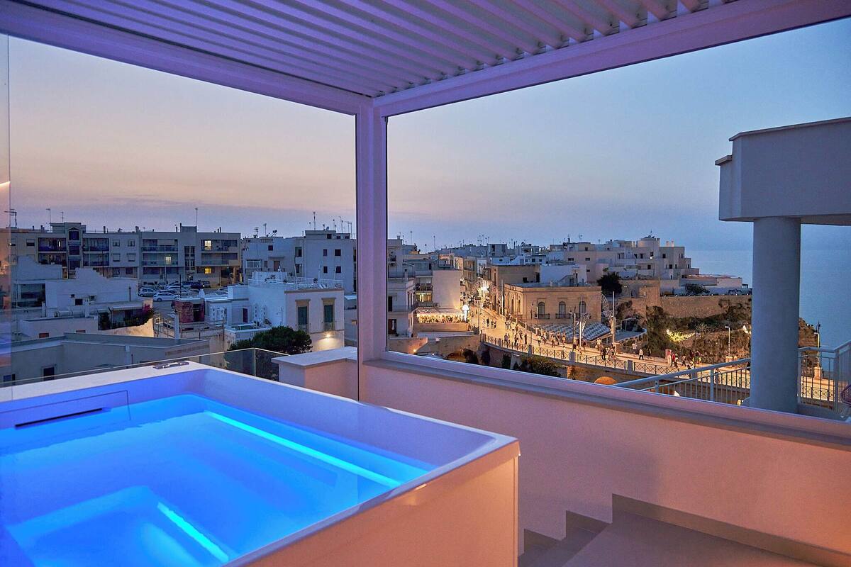 A rooftop pool with a view of a coastal town at dusk.