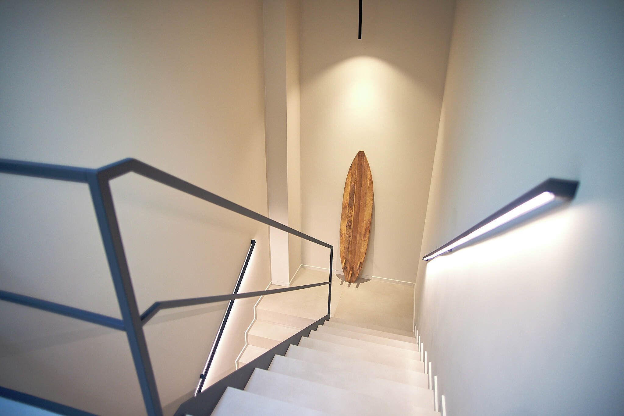 A staircase with a wooden sculpture at the top, a metal handrail, and a light fixture on the wall.
