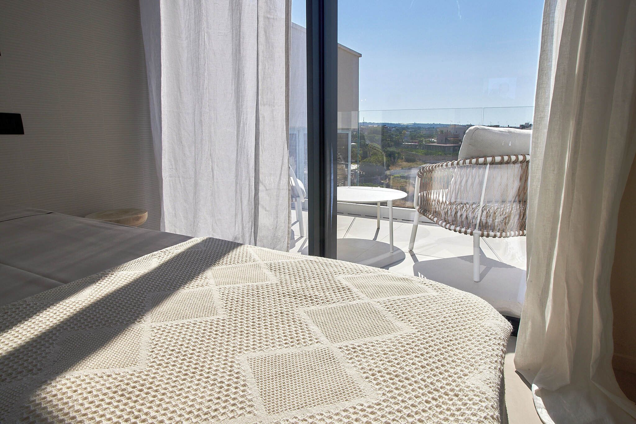 Een slaapkamer met een groot bed, uitzicht op het landschap door een raam en een balkon met een stoel en tafel.